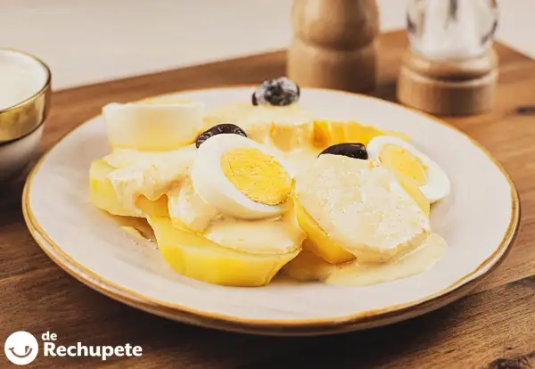 Papa a la huancaina servida en un plato blanco, con rodajas de huevo duro y aceitunas negras.