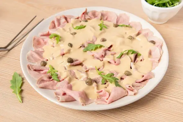 Delicioso vitello tonnato con finas lonchas de ternera, salsa cremosa, alcaparras y rúcula. Un plato italiano clásico.