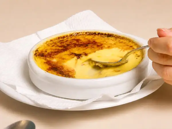 Una cuchara se hunde en un cremoso creme brulee con una capa superior caramelizada y dorada.