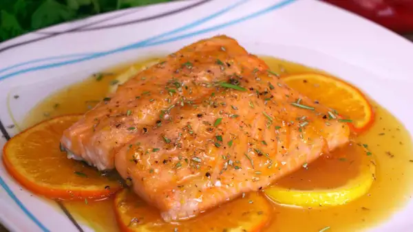 Delicioso salmón a la naranja, bañado en salsa cítrica y adornado con rodajas de naranja y hierbas frescas.
