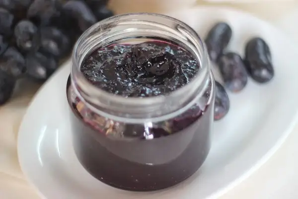 Frasco de mermelada de uvas casera, con uvas frescas al lado. Un dulce manjar para disfrutar.