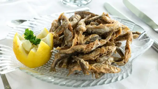 Deliciosa fritura de pescado crujiente servida en un plato con forma de pez, acompañada de limón tallado y perejil fresco.