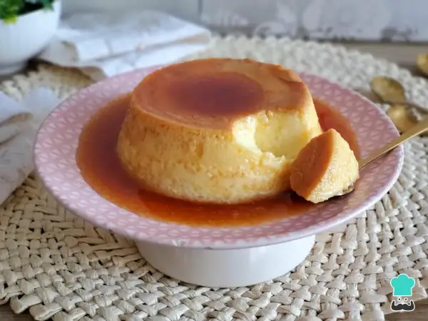 Un delicioso flan de leche condensada, con una porción servida en cuchara dorada, bañado en caramelo líquido.