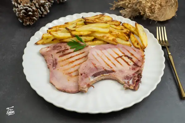 Dos chuletas de sajonia a la parrilla con patatas fritas y perejil. Un plato delicioso y listo para disfrutar.