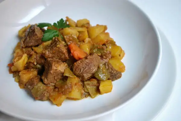 Un plato de carne guisada con patatas, zanahorias y pimientos verdes, adornado con perejil fresco.