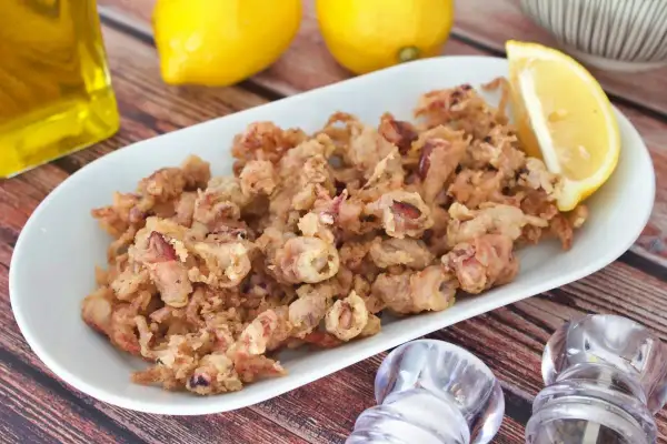 Crujientes puntillas de calamar fritas, servidas en plato blanco con limón y aceite de oliva.